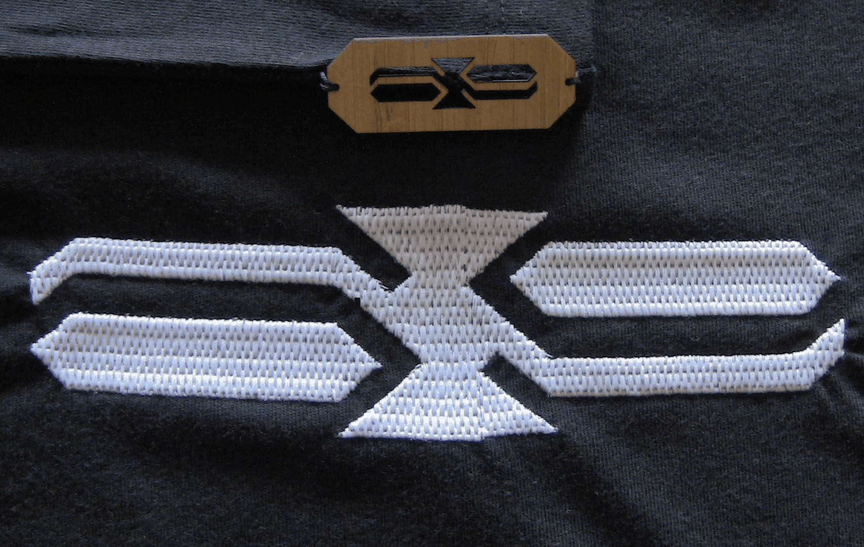 White geometric logo on black fabric with a wooden tag above.