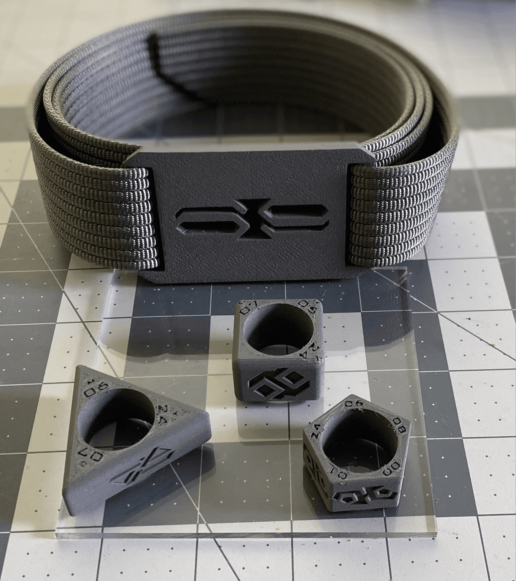 Rolled-up gray tactical belt with a unique clasp design, accompanied by three geometric dice accessories.